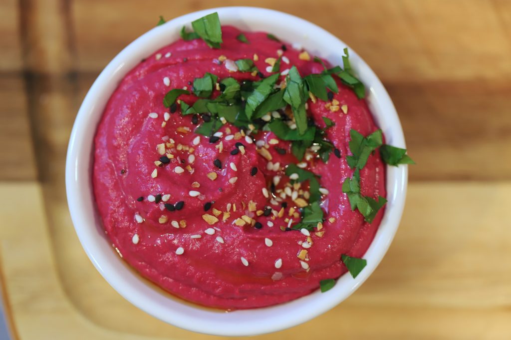 Vibrant pink roasted beet hummus in dish garnished